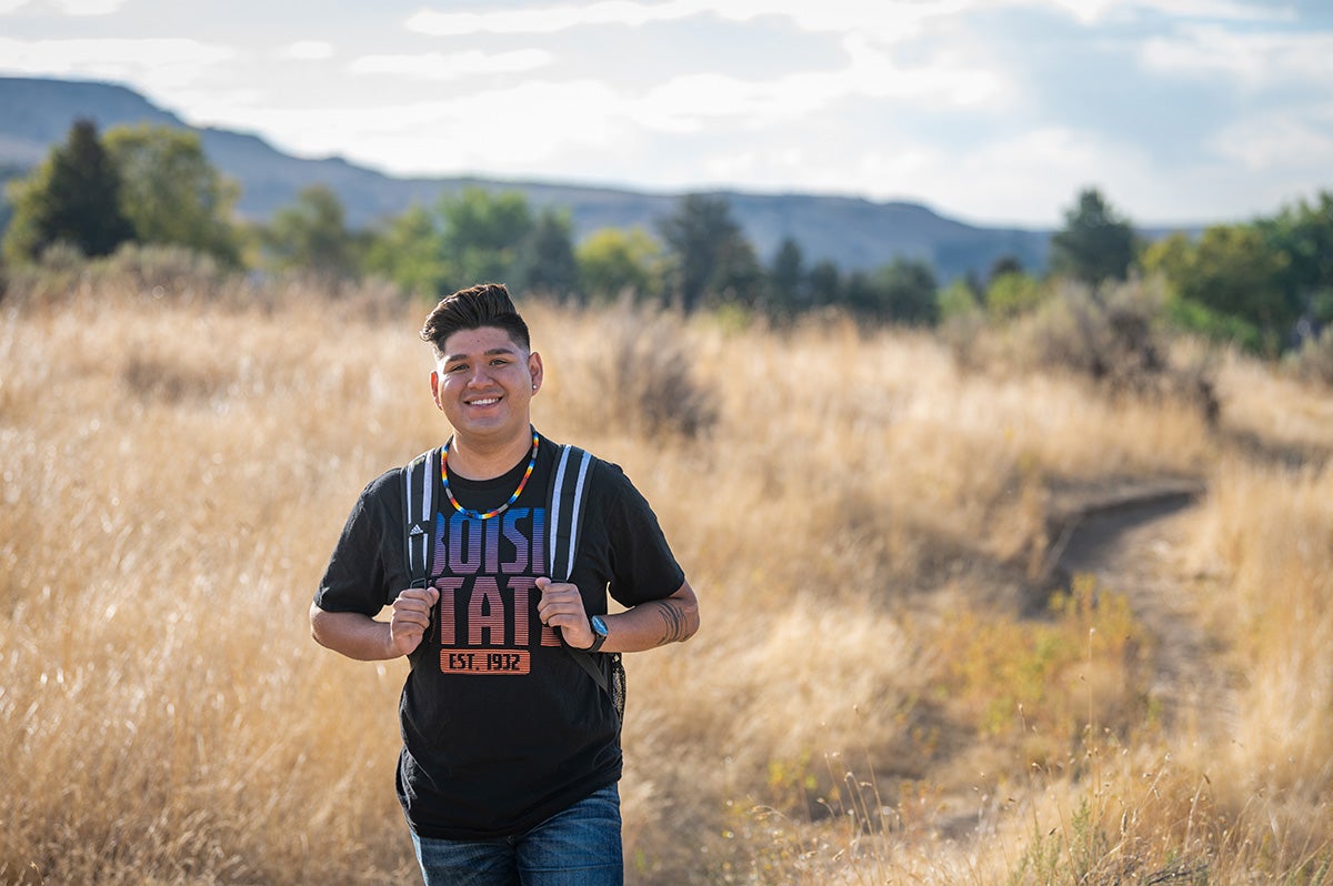 Marco smiles and stands in a field with his backpack over his shoulder.