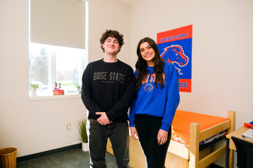 Two students wearing Boise State sweatshirts standing in a dorm room.