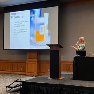 Dr. Cynthia Curl presenting at a podium on urinary biomonitoring