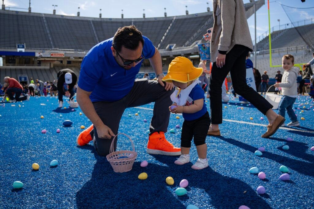 A man helps a baby pick up Easter eggs on the football field