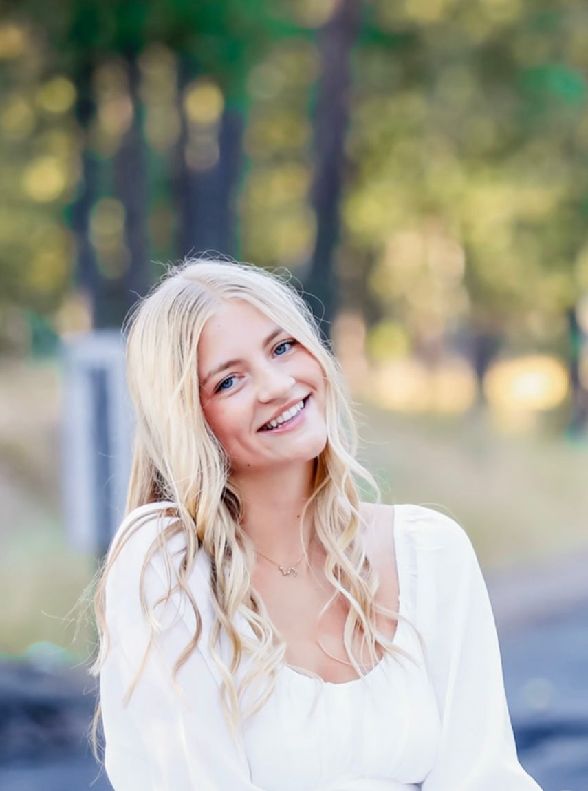 Summer Bates wearing a radiant white top smiling at the camera in front of a grove of trees