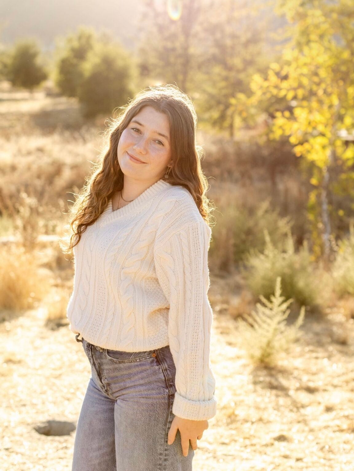 Alana Heusser standing in a desert field with trees in the background, smiling