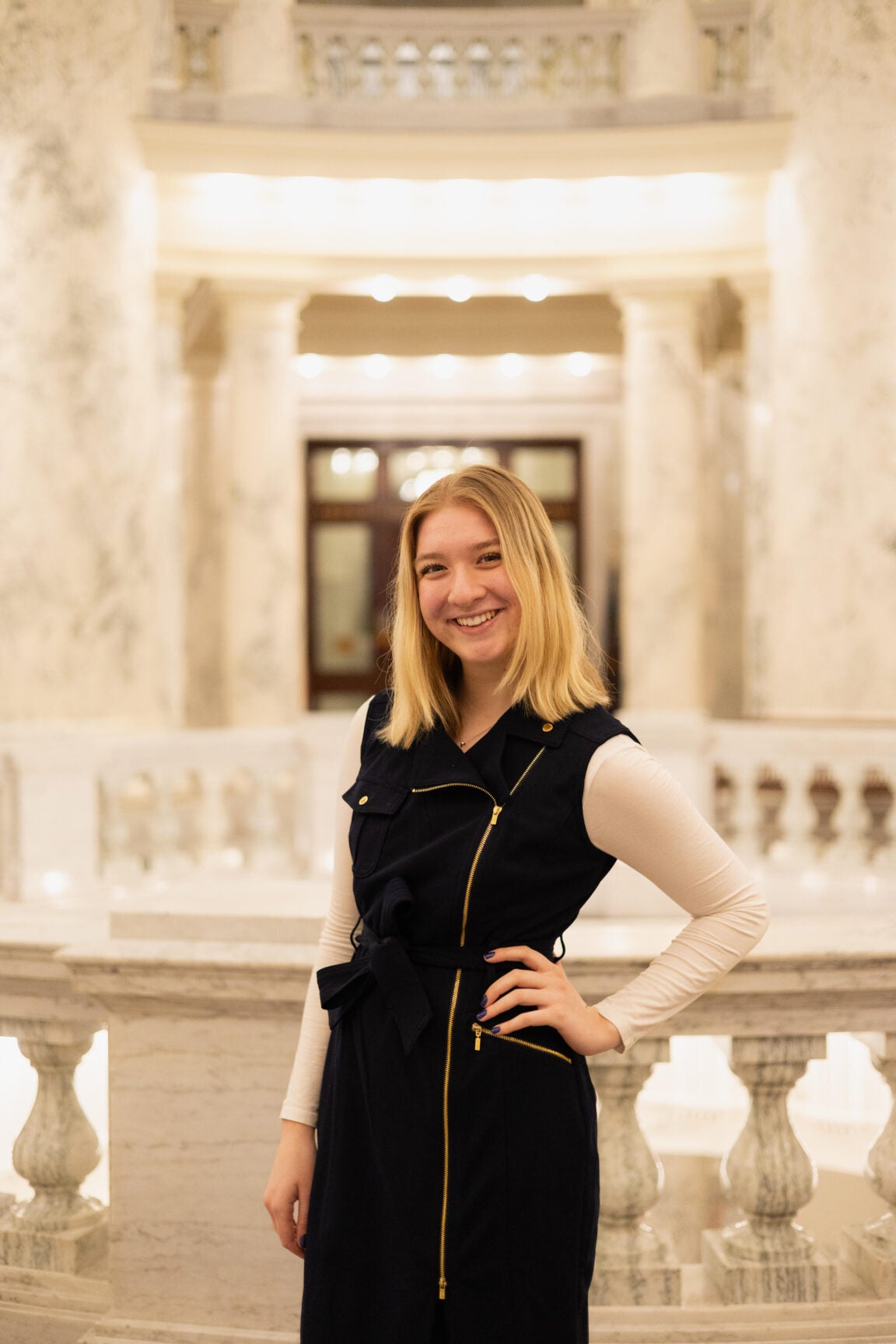 Emilia Nowinski standing in the Idaho Capitol Rotunda, smiling, with her hand on her hip