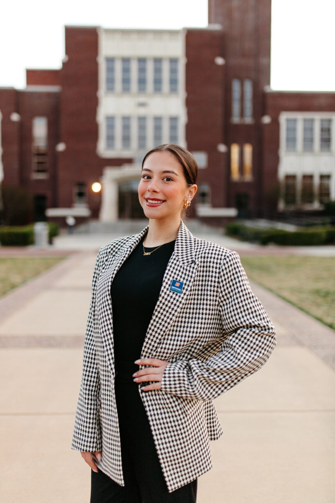 Emia Venegas standing with her hand on her hip, smiling, in front of a brick building
