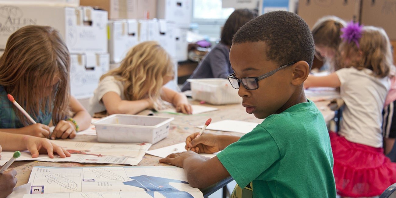 A group of children are seated at a table, engaged in an activity that involves writing or drawing.