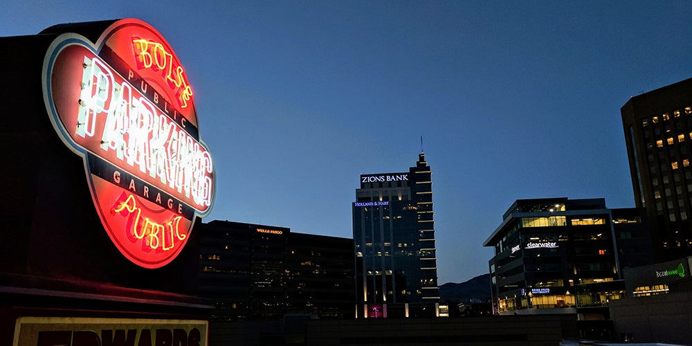 A neon sign reads Boise Public Parking Garage at nighttime, surrounded by tall buildings