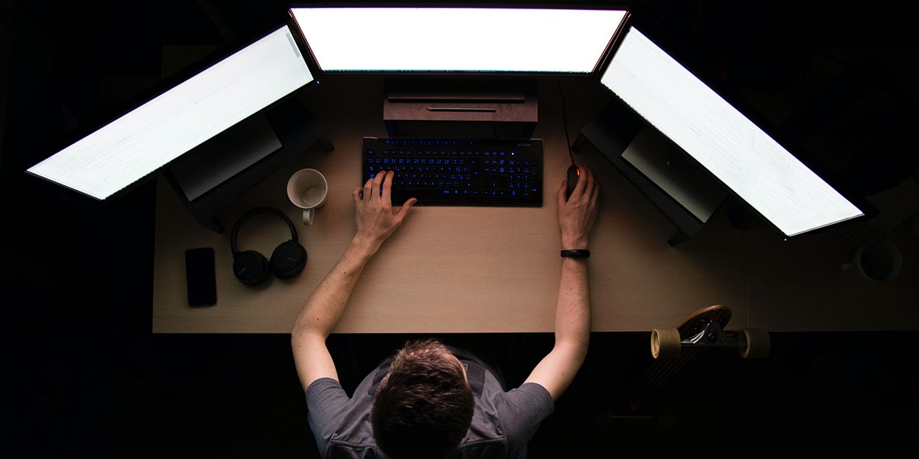 A man sits at a desk with three computer monitors 