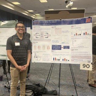 Nic Hunt stand in front of his poster at the 2024 Graduate Student Showcase