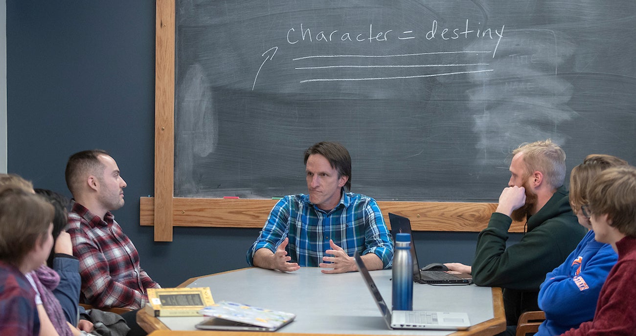 Group of students sitting around a table listening to an instructor, a chalk board behind them says character equals destiny