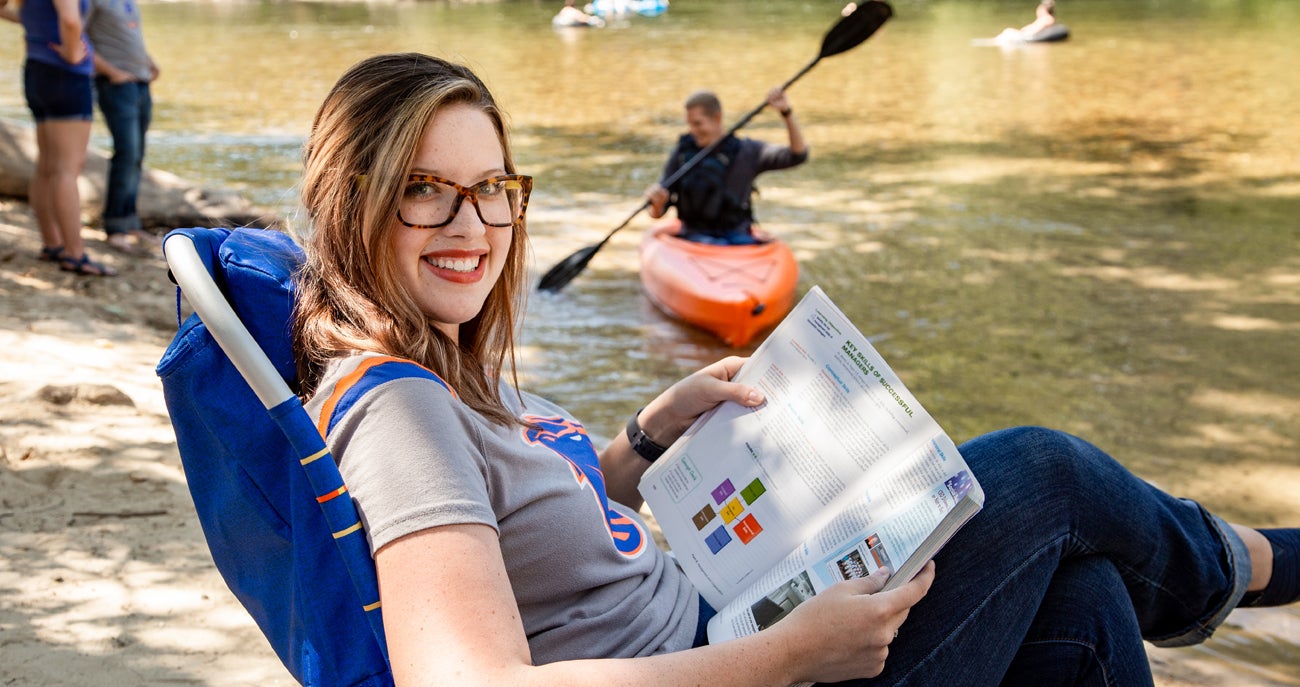 A student reads a textbook along the Boise river.