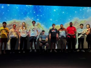 Group of students standing in front of projected photo of space