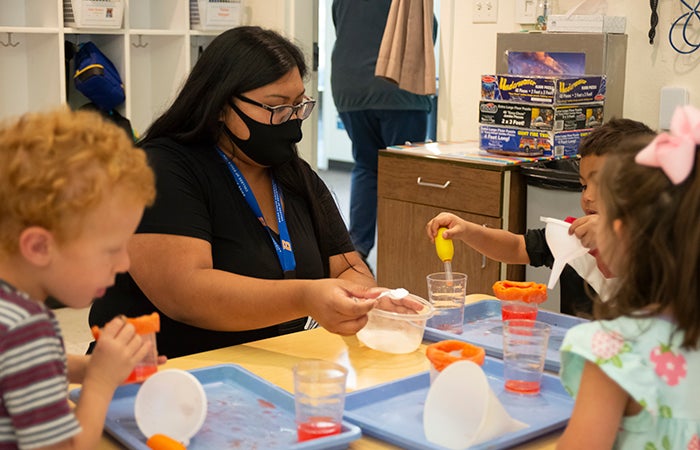 Teacher wearing facial covering working with children at a table