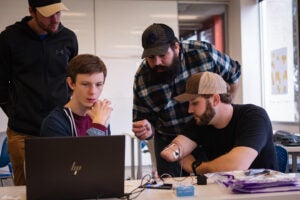 Three male students testing a prosthetic arm on a student in need.