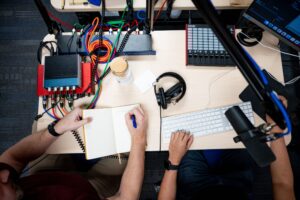 An arial view of two students working at a recording desk, with a soundboard nearby.