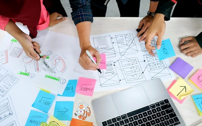 Team working on a project, with sticky notes and graphics, laptop in the center of the table