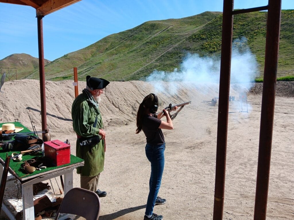 A volunteer oversees a Boise State student firing a historical weapon.