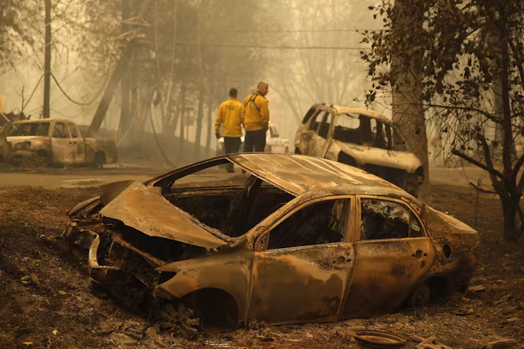 Firefighters inspect burned out cars along a road in Paradise, California