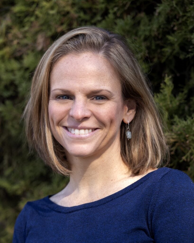 Brittany Brand smiling in navy blue shirt in front of green trees.