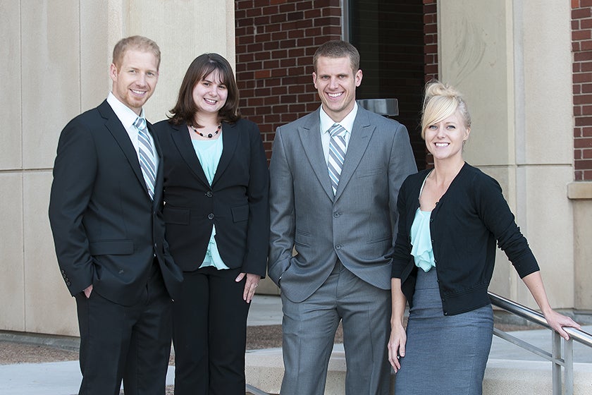 Four students stand in front of business building