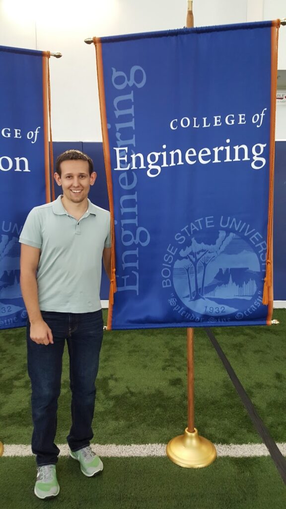 Photo of Dan Kondratyuk standing to the left of a College of Engineering sign from Boise State University.