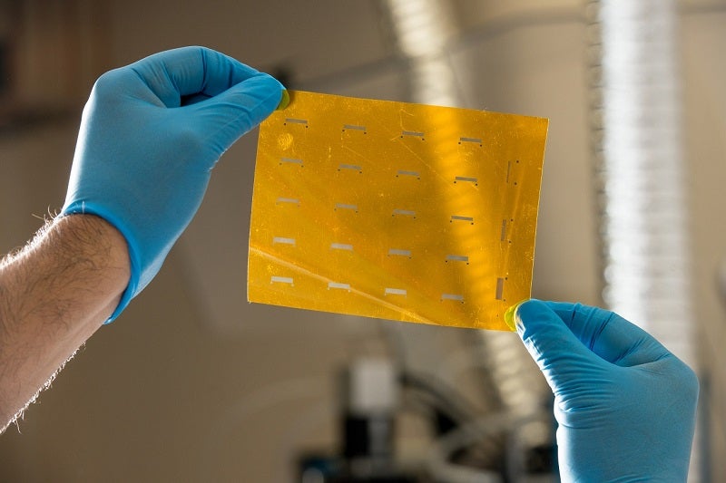 pair of gloved hands is holding a thin, rectangular sheet of yellow material