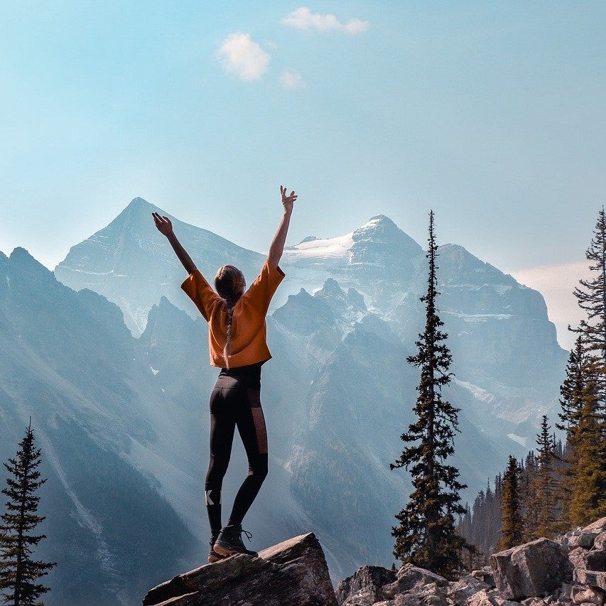 person reaching to the sky in the mountains