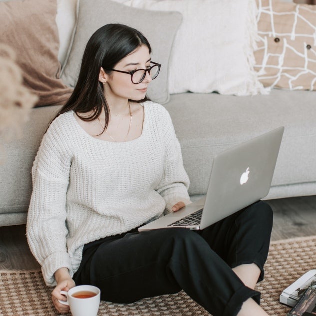 girl in sweater seated on floor with a laptop