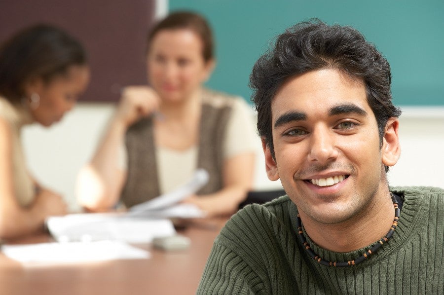 male student facing us with two female students working at a desk behind him