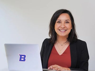A student posing with an open laptop with the Boise State logo on it