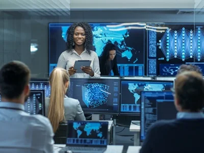 Several people in a technology room with multiple monitors with technical graphics