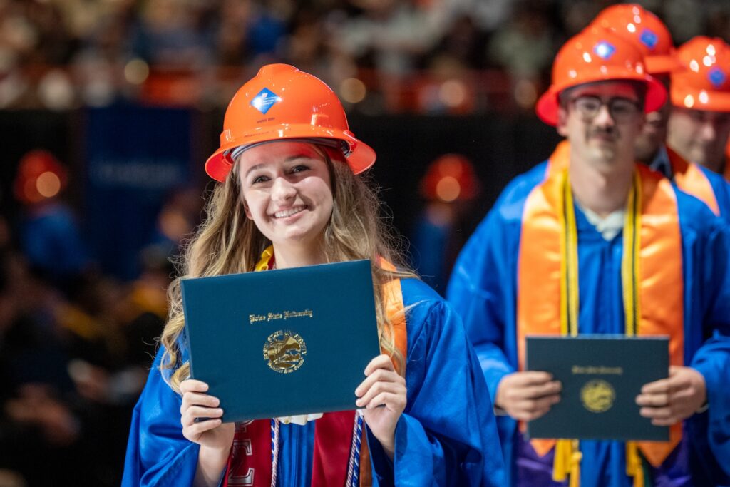 graduate with orange hart hat on smiling and holding a diploma