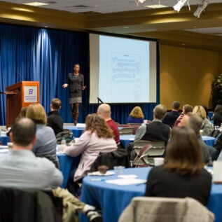 Speaker on stage engages with audience at round tables