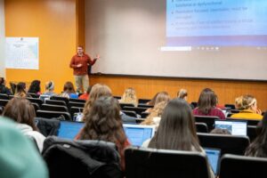 A professor gives a presentation in front of a full class. 