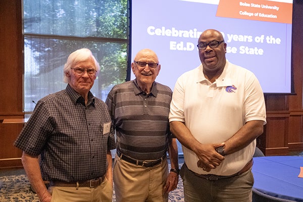3 gentlemen who are alumni posing for a picture together in front of a seminar