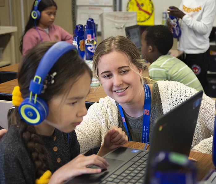 Student teacher working with an elementary student at a computer