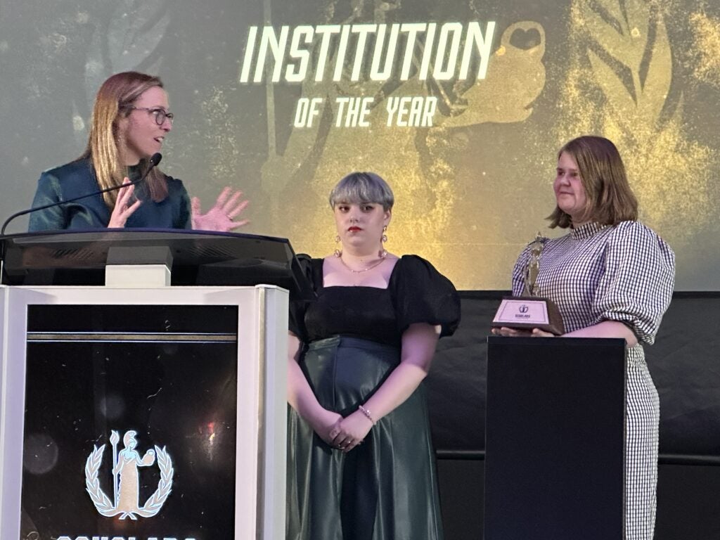 Three people stand on stage, one is holding an award
