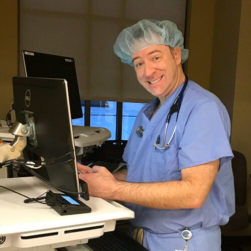 Dr. Gary Jauregui, dressed in scrubs, smiles and looks at a computer screen in a medical setting
