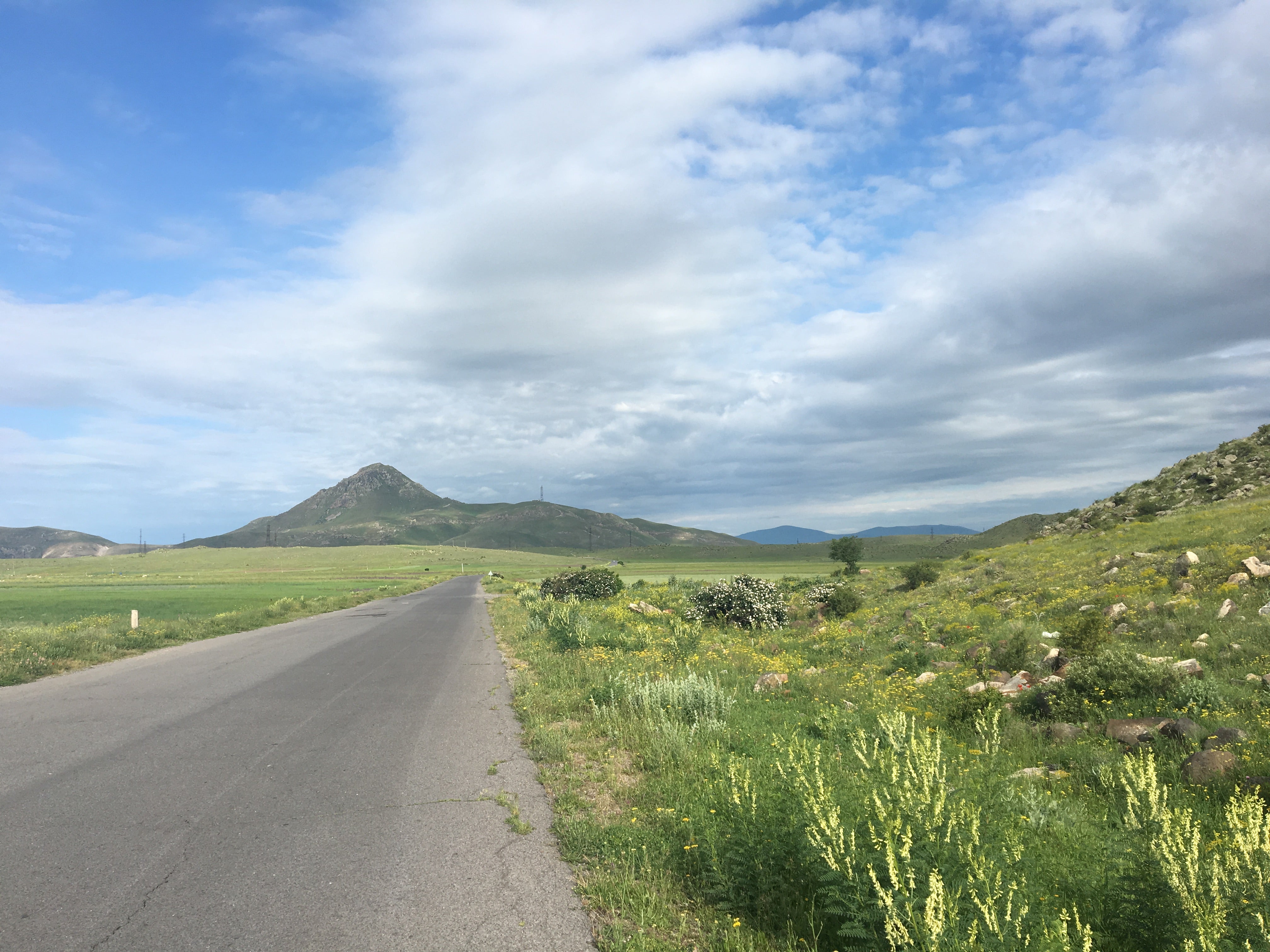 Landscape of green hills, with a paved road leading to a mountain. 