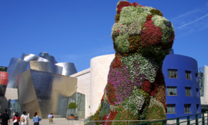 Large colorful floral dog sculpture, modern Guggenheim Museum Bilbao backdrop. Renowned art and architecture.