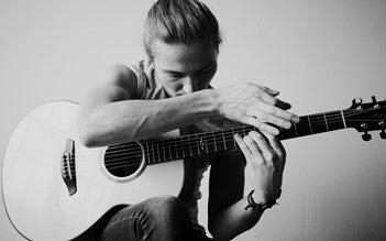 Black and white photo of artist Calum Graham playing an acoustic guitar