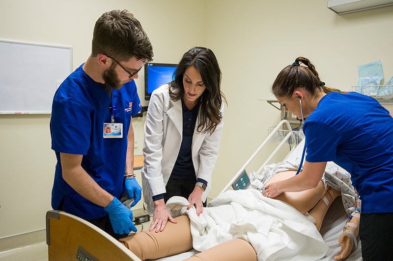 Professor and student practice patient care on a manikin