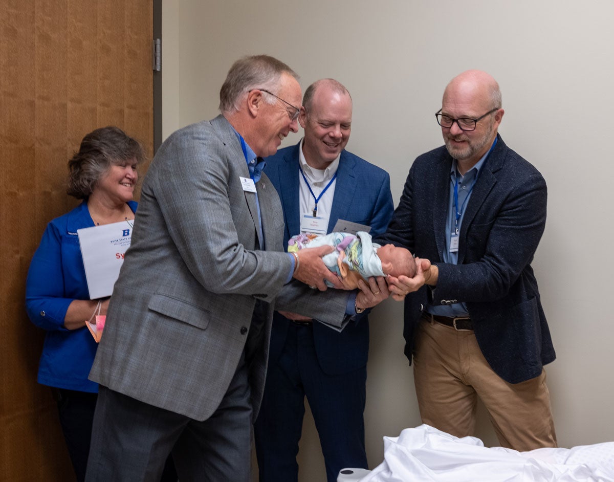 A group of men carefully pass a manikin baby between them while a tour guide looks on.