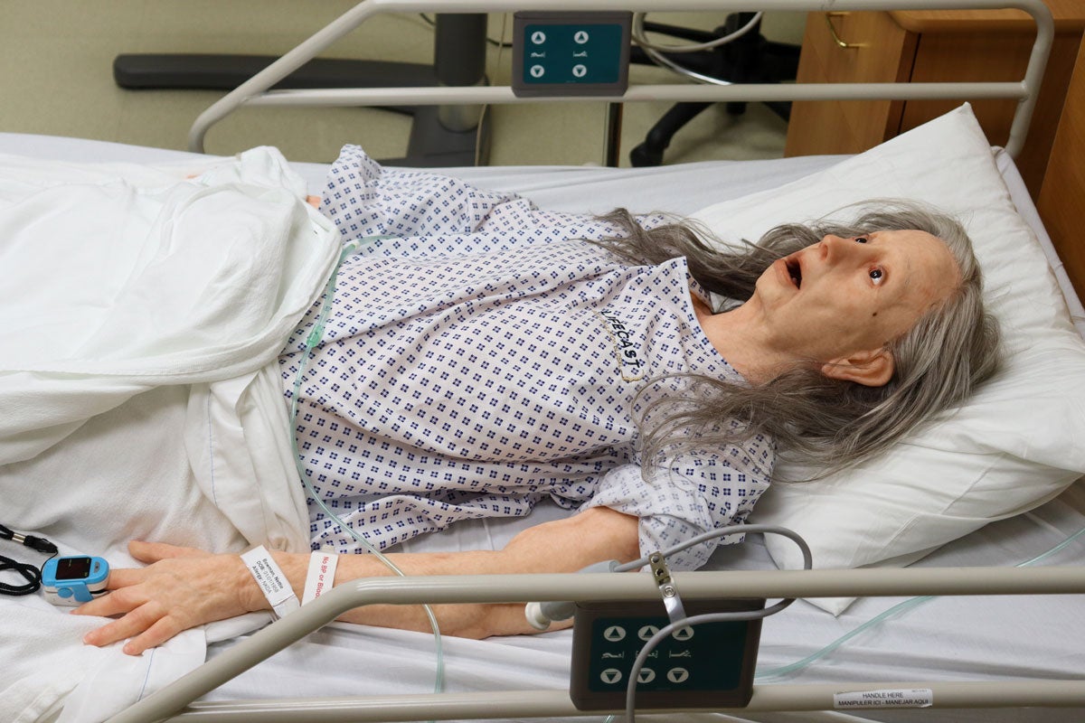 An elderly high visual fidelity manikin lies on a gurney.