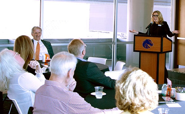Jo Powers, incoming dean for the College of Health Sciences, standing at a podium giving a roast to outgoing Tim Dunnagan at his recognition event surrounded by his colleagues. 