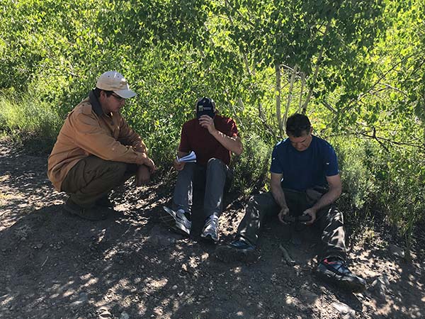 three men site on a trail in the shade