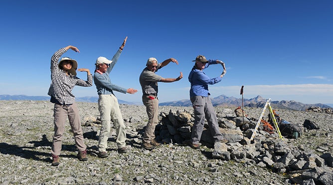 People spelling GLORIA with their arms and other props on mountain summit