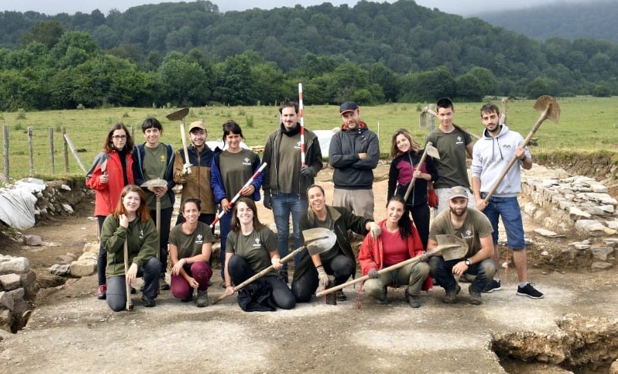 Group photo of students and staff holding shovels at excavation site.