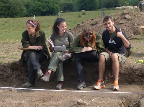 4 students sitting on sideline of an excavation site.
