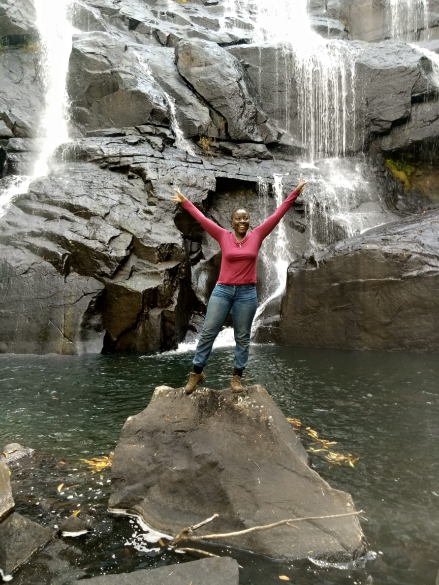 Domingas Matlombe joyfully poses near a waterfall