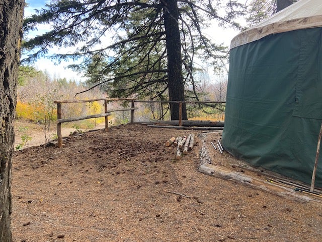 the new railings are partially finished but still missing some croassbars. a pile of logs sits nearby and the edge of the green songbird banding yurt is partly visible